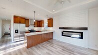 This single-floor, 2-bedroom, 2-bathroom home at 10 Candlelight Plz offers a thoughtfully designed layout that maximizes functionality and style. The open-concept kitchen and living area serves as the heart of the home, showcasing warm honey-toned wood cabinetry, quartz countertops, and a large center island with pendant lighting overhead. Stainless steel appliances, including a gas range and French door refrigerator, complement the stainless farmhouse sink. Light wood-look flooring runs throughout the common areas, while a shiplap-clad fireplace with a sleek black surround anchors the living space. A ceiling fan adds comfort to the area. Both bedrooms feature plush carpet, crown molding, natural light from windows, and closet access, creating comfortable and private retreats. Three closets provide ample storage throughout the home. The two bathrooms are finished with warm wood cabinetry and matte black hardware; one features a tub-shower combo while the other offers a walk-in shower with a glass enclosure. Light wood-look tile flooring ties the bathrooms together with the rest of the home's cohesive aesthetic. A connecting hallway links the bedrooms and bathrooms efficiently, completing this well-organized floor plan.