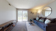 Located at 7200 Chadwood Ln in Dublin, Ohio, this single-floor residence offers a well-organized layout designed for comfortable everyday living. The living room serves as the centerpiece of the home, featuring plush carpeting, a textured ceiling, and a full-width sliding glass door that floods the space with natural light and provides direct access to an outdoor patio with green views beyond.

The galley-style kitchen is efficiently arranged with warm wood cabinetry lining both sides, dark granite-style countertops, hardwood-style flooring, and black appliances including a range and dishwasher. A door at the end of the kitchen leads to an in-unit laundry area, adding everyday convenience.

The bedrooms are carpeted and well-lit, with large windows that invite natural light. The primary bedroom includes a walk-in closet and its own private bathroom, which features a wood-toned vanity with a granite-style countertop and a shower-tub combination. A second full bathroom mirrors this style, maintaining a cohesive aesthetic throughout. A dedicated office room with carpeting and a window provides a functional workspace.

The overall ambiance of the home is neutral and understated, with soft gray walls, consistent flooring materials, and a clean, move-in ready presentation throughout.