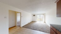 This single-floor residence offers a thoughtfully designed layout that balances comfort and functionality. The spacious living area is finished with plush carpeting and light tile flooring near the entryway, creating a welcoming transition between spaces. A wall-mounted air conditioning unit and baseboard heating ensure year-round comfort, while a large sliding glass door floods the room with natural light and provides direct access to an outdoor balcony with views of surrounding greenery.

The kitchen is a standout feature, showcasing rich cherry wood cabinetry, dark granite countertops, and a classic tile backsplash. A full suite of stainless steel appliances — including a refrigerator, range, microwave, and dishwasher — is complemented by track lighting overhead and generous storage throughout. Light tile flooring ties the kitchen together cleanly.

The bedroom is a comfortable retreat, carpeted and bright, with a ceiling fan with integrated light fixture and a window that allows natural light to filter in. A baseboard heater ensures warmth during cooler months.

The bathroom features full tile surround walls with decorative diamond tile accents, a soaking bathtub with overhead shower, and coordinating fixtures. The vanity area, visible in the floor plan, includes dual mirrors and warm wood cabinetry, adding a refined touch to the space.