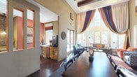 This single-floor community clubhouse is thoughtfully designed to provide an inviting and versatile gathering space. The entrance greets visitors with a dramatic foyer featuring dark slate tile flooring, a bold round accent table, and tall decorative plants that set an elegant tone. Soaring double-height ceilings and floor-to-ceiling windows define the main lounge areas, flooding the interiors with abundant natural light and offering views of the surrounding landscaping, including mature palm trees.

The main lounge is anchored by a striking full-height brick fireplace with a wall-mounted television above, complemented by warm terracotta accent walls, colorful area rugs, and an eclectic mix of seating including leather chairs, upholstered sofas, and accent armchairs. Dramatic draped curtains frame the expansive windows, adding depth and warmth to the space.

A dedicated games room features a full-size pool table, a shuffleboard table, and a wall-mounted television, making it an ideal space for recreation and socializing. A compact beverage station with granite countertops, cabinetry, and a water dispenser provides added convenience. Throughout the space, curated artwork, layered lighting, and cohesive earth-toned décor create a welcoming and polished communal atmosphere.