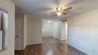 This single-floor, one-bedroom, one-bathroom unit offers an efficient and thoughtfully organized layout. The living room features rich, dark hardwood-style flooring and a ceiling fan with light fixture, creating a comfortable and functional space. A striking dark brick accent wall serves as a dramatic focal point, adding character and warmth to both the living area and additional rooms throughout the unit. The galley-style kitchen is well-appointed with light wood cabinetry, granite-look countertops, a white electric range, and a refrigerator. A window at the end of the kitchen brings in natural light, enhancing the open feel of the cooking space. The bedroom is carpeted for comfort and includes its own ceiling fan, a window with exterior views, and a prominent brick accent wall that ties the space together cohesively. The bathroom features tile flooring, a vanity with granite countertop, light wood cabinetry, and a shower-tub combination. A dedicated closet provides built-in shelving along both walls with hardwood-style flooring, offering practical storage. A hallway connects the rooms, completing this compact yet functional single-level layout.