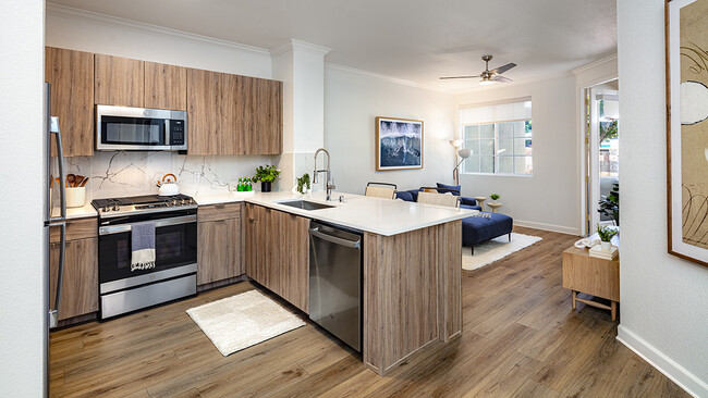 Apartment kitchen with stainless steel appliances, dining and living room with wood-style flooring. - Griffis South Bay