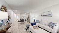 This single-floor unit offers a clean, contemporary design characterized by a crisp white color palette, light wood-look flooring, and an open-concept layout that seamlessly connects the living, dining, and kitchen areas. Recessed lighting and large windows allow natural light to fill the space, enhancing its airy, welcoming atmosphere.

The living area provides a comfortable gathering space with large windows overlooking a landscaped outdoor area, offering pleasant garden views. The kitchen is well-appointed with white shaker-style cabinetry extending to the ceiling, light quartz countertops, and a full suite of stainless steel appliances including a refrigerator, range, microwave, and dishwasher. The adjacent dining area accommodates a small table, making everyday meals convenient.

The bedroom features wide windows that bring in generous natural light and offer outdoor views, complemented by soft carpeting for added comfort. The full bathroom is finished with large-format marble-look tile flooring, a tub-shower combination, and a white vanity with ample storage. A louvered closet provides additional organization space. Overall, the unit presents a cohesive, modern aesthetic throughout.