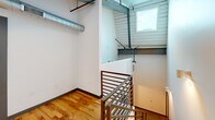This two-story apartment at 144 4th St, Apt 240, Burlington, NC offers a compact yet efficiently designed layout spread across two levels. The main floor features a modern kitchen equipped with rich dark-wood cabinetry, granite countertops, stainless steel appliances including a refrigerator, range, microwave, and dishwasher, set atop polished concrete flooring. The upper loft level showcases warm hardwood flooring, exposed industrial ductwork, and an open-railing staircase, lending the space a distinctive urban character. A skylight window brings in natural light. The bathroom includes a granite-topped vanity, hardwood floors, and a tub-shower combination.
