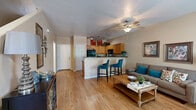 This two-story residence offers a well-organized layout across two floors, with the main living areas occupying the lower level and the bedrooms situated above. The ground floor features an open-concept kitchen and living room combination with warm hardwood-style flooring throughout. The kitchen is outfitted with light maple cabinetry, dark granite-style countertops, black appliances including a refrigerator, range, and microwave, and a peninsula breakfast bar with bar stool seating — ideal for casual dining. Track lighting above the kitchen enhances functionality, while a ceiling fan with light fixture serves the living room area. The living room is bright and welcoming, with a window that invites natural light. A dedicated laundry room with a full-size washer and dryer adds everyday convenience on this level. Upstairs, the primary bedroom is a comfortable retreat featuring plush carpet, a ceiling fan, and a door providing access to a private exterior balcony or patio. The second bedroom also offers carpeted flooring and ample space. All three bathrooms are well-appointed, featuring tub-shower combinations, warm wood vanities with dark countertops, and hardwood-style flooring. A closet and staircase complete the home's thoughtfully designed floor plan.