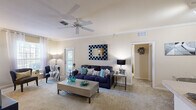 This single-story, 3-bedroom, 2-bathroom residence offers a thoughtfully organized layout across a comfortable footprint. The open living room is a welcoming focal point, featuring plush carpeting, crown molding, a ceiling fan, and natural light from exterior-facing windows and a glass door. The galley-style kitchen is outfitted with dark espresso cabinetry, light countertops, tile flooring, and black appliances including a range, microwave, refrigerator, and dishwasher. A dedicated laundry room with side-by-side washer and dryer hookups adds everyday convenience. The primary bedroom is a generously sized retreat with large windows that allow ample natural light and outdoor views, complemented by soft carpeting and direct access to its en-suite bathroom. The en-suite features a wide vanity with dual mirrors and a well-appointed shower area. The secondary bedrooms are comfortably sized with carpeted floors and natural light. The second bathroom includes a tiled tub-shower combination, a vanity, and classic tile flooring. Two closets and a hallway complete the layout, providing practical storage solutions throughout this efficiently designed residence.