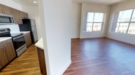 This well-designed single-floor residence offers a clean, contemporary aesthetic anchored by rich hardwood-style flooring and neutral-toned walls throughout the main living areas. The open-concept kitchen serves as a central hub, featuring a large white quartz island with an undermount sink, walnut-toned cabinetry extending floor to ceiling, bright white countertops, and a full suite of stainless steel appliances including a refrigerator, range, and built-in microwave. Recessed lighting illuminates the kitchen and adjacent living space, which flows seamlessly toward a windowed wall offering urban views.

The living area is generously proportioned, with large multi-pane windows on two walls that flood the space with natural light and frame exterior city and hillside views. A hallway connects the living zone to the bedrooms, each carpeted and well-lit by oversized windows. One bedroom features sliding glass doors opening to a balcony with expansive city views, while another benefits from a large picture window with similar scenic sightlines.

The bathrooms are finished to a high standard, with one featuring a marble-veined quartz vanity top, a wide frameless mirror, and a tub-shower combination, while a second bathroom includes wood-toned cabinetry and hardwood-style flooring. In-unit laundry connections are also present, adding practical convenience to this polished, light-filled residence.