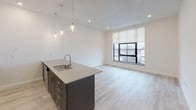 Located on College Avenue in Rochester's vibrant East End neighborhood, this single-floor unit offers a clean, contemporary design with high-quality finishes throughout. The open-concept kitchen and living area serves as the centerpiece of the space, anchored by a sleek island with a quartz countertop, undermount sink, and dark espresso cabinetry. Stainless steel appliances, a mosaic tile backsplash, white upper cabinets, and pendant lighting complete the kitchen's modern aesthetic. Light hardwood-style flooring runs seamlessly throughout, lending warmth and continuity to every room. Large, black-framed windows fill each room with natural light and provide views of the surrounding Rochester neighborhood. The living area is generously proportioned, offering a bright and open atmosphere. The bedrooms are well-sized, featuring the same light flooring, neutral white walls, and oversized windows with roller shades for privacy. The bathroom is elegantly appointed with a walk-in glass shower featuring a rain showerhead, dark vanity cabinetry with quartz counters, a large mirror, and crisp tile flooring. Throughout the unit, the design emphasizes clean lines, a neutral palette, and modern fixtures, creating a cohesive and move-in-ready living environment.