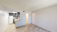 Located at 2912 East Indian School Road in Phoenix, Arizona, this efficient single-floor unit offers a well-designed layout comprising a combined living and kitchen area alongside a full bathroom. The living space is anchored by light-toned wood-look flooring that runs throughout, complemented by crisp white walls and a textured popcorn ceiling that adds a classic residential character. Natural light filters in through a window fitted with vertical blinds near the front entry door, keeping the space bright and welcoming.

The kitchen is seamlessly integrated into the living area via a peninsula-style counter with a light granite surface, providing additional workspace and a casual dining option. Gray cabinetry with a modern flat-front profile lines the kitchen walls, paired with a tile backsplash and a skylight above that enhances natural illumination. A white refrigerator and electric range complete the functional appliance lineup.

The bathroom features a clean, updated aesthetic with a white vanity cabinet topped by a speckled granite countertop and an undermount sink. Brushed nickel fixtures and a framed mirror add a polished touch, while the bright overhead lighting ensures excellent visibility. The layout is practical and efficiently appointed throughout, making this a well-maintained unit suited for streamlined urban living in the heart of Phoenix.