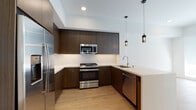 Located at 6606 Variel Ave in the Canoga Park neighborhood of Los Angeles, this contemporary single-floor residence offers a well-designed layout with modern finishes throughout. The kitchen is a standout feature, showcasing rich dark wood cabinetry that extends floor to ceiling, complemented by a crisp white chevron-patterned tile backsplash and light quartz countertops. Stainless steel appliances — including a gas range, over-the-range microwave, refrigerator, and dishwasher — complete the space, while stylish pendant lighting adds a refined touch. Light hardwood flooring flows seamlessly from the kitchen into the open living area, creating a cohesive and airy feel. A dedicated laundry closet with stacked washer and dryer units provides added convenience just off the main living space. The bedroom features neutral carpet flooring, clean white walls, and a window fitted with blinds that allows natural light to filter in. The bathroom is finished in a clean, minimalist style with floor-to-ceiling white tile surrounding the shower-tub combo, light stone-look tile flooring, and built-in open shelving for storage. Recessed lighting and a neutral color palette throughout lend the space a bright, move-in-ready atmosphere.