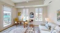 Located at 2613 Montgomery St in the heart of Savannah, GA, this thoughtfully designed one-bedroom, one-bathroom residence offers a bright and efficient single-floor layout. The living room is bathed in natural light streaming through large windows with roller shades, showcasing light hardwood flooring, a tray ceiling with a ceiling fan, and a warm, inviting ambiance. A dining area nestled within the living space features a glass-top table with vibrant yellow accent chairs, adding a cheerful pop of color. The open layout also reveals a well-appointed kitchen visible from the main living area, fitted with light cabinetry and modern appliances. The spacious bedroom benefits from multiple windows on two walls, filling the room with natural light and offering views of the surrounding greenery. A ceiling fan, light hardwood floors, and ample wall space complete the comfortable retreat. The full bathroom is a standout feature, boasting a long, sleek vanity with teal-blue cabinetry, a white countertop with dual sinks, a large framed mirror, and dual windows that provide excellent natural light and ventilation. Large-format floor tiles add a clean, contemporary touch. A connecting hallway ties each room together cohesively, making this residence a polished and functional home in a prime Savannah location.