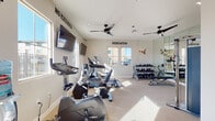 This fitness center, located in Brentwood, CA (94513), is a thoughtfully designed single-level facility offering a comprehensive workout environment. The room is finished with neutral-toned walls and light carpeted flooring, creating a clean and functional atmosphere. Multiple windows allow abundant natural light to fill the space, providing views of the surrounding community.

The cardio area is well-stocked with Spirit-brand upright and recumbent exercise bikes, an elliptical cross-trainer, and a treadmill, all equipped with individual display screens. Two wall-mounted flat-screen televisions are positioned for easy viewing during workouts. A pair of ceiling fans helps maintain comfortable airflow throughout the room.

The strength training section features a Spirit dual-stack functional trainer, ideal for cable-based exercises, along with a tiered dumbbell rack stocked with a full range of free weights. A large wall mirror in the strength area enhances the sense of space and allows users to monitor their form.

Motivational wall decals reading "NO EXCUSES" and "DEDICATION" contribute to an energizing atmosphere. A large wall clock and a direct-access door to the outdoor area add convenience. The overall design is practical, well-lit, and conducive to a focused fitness routine.