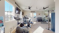 This fitness center, located in Brentwood, CA (94513), is a thoughtfully designed single-level facility offering a comprehensive workout environment. The room is finished with neutral-toned walls and light carpeted flooring, creating a clean and functional atmosphere. Multiple windows allow abundant natural light to fill the space, providing views of the surrounding community.

The cardio area is well-stocked with Spirit-brand upright and recumbent exercise bikes, an elliptical cross-trainer, and a treadmill, all equipped with individual display screens. Two wall-mounted flat-screen televisions are positioned for easy viewing during workouts. A pair of ceiling fans helps maintain comfortable airflow throughout the room.

The strength training section features a Spirit dual-stack functional trainer, ideal for cable-based exercises, along with a tiered dumbbell rack stocked with a full range of free weights. A large wall mirror in the strength area enhances the sense of space and allows users to monitor their form.

Motivational wall decals reading "NO EXCUSES" and "DEDICATION" contribute to an energizing atmosphere. A large wall clock and a direct-access door to the outdoor area add convenience. The overall design is practical, well-lit, and conducive to a focused fitness routine.