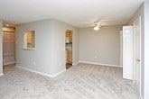 This single-floor residence offers a comfortable and functional layout with a neutral color palette throughout. The living room serves as the heart of the space, featuring plush wall-to-wall carpeting, a fireplace with a clean white mantel, and a set of French doors flanked by windows that invite natural light and provide access to an outdoor area. The open floor plan connects the living room to a dining or flex area, with a pass-through architectural cutout that links seamlessly to the kitchen. The galley-style kitchen is efficiently designed with light wood cabinetry, white appliances including a refrigerator, electric range, microwave, and dishwasher, complemented by a double-basin sink and light wood-look flooring that contrasts the carpeted living areas. The bedrooms are generously sized, each featuring soft carpeting, neutral walls, and ample natural light from well-positioned windows. One bedroom includes direct access to a walk-in closet or utility area. The bathroom features a single-sink vanity with light wood cabinetry, white countertops, a large wall mirror with overhead lighting, and wood-look flooring, providing a clean and practical finish. Textured ceilings and consistent neutral tones throughout lend the space a cohesive, move-in-ready ambiance.