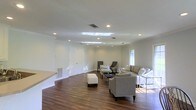 Located at 3975 I-55 N in Jackson, Mississippi, this single-floor space offers a clean, modern aesthetic with a thoughtfully designed open layout. The main living area is expansive and inviting, anchored by rich, dark hardwood flooring that runs throughout and provides a warm contrast to the crisp white walls and trim. Recessed lighting is installed across the ceiling in a deliberate arrangement, ensuring even, ambient illumination throughout the space. A notable skylight feature adds an additional source of natural light, brightening the interior and creating an airy atmosphere. Crown molding along the upper edges of the walls adds a refined architectural detail. The open floor plan allows for flexible furniture arrangements, as demonstrated by the generously sized seating area that accommodates multiple conversation zones. A raised platform or built-in counter element along one wall offers functional versatility. Windows along the perimeter invite natural light and views of the surrounding exterior. The overall ambiance is polished and neutral, making the space highly adaptable for a variety of uses. The combination of contemporary finishes, thoughtful lighting design, and open, flowing layout makes this a well-appointed and functional property.
