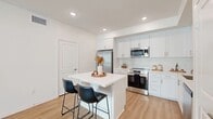Located at 550 E Foothill Blvd in Rialto, California, this well-appointed single-story, 3-bedroom, 2-bathroom home offers a clean, modern aesthetic throughout. Light wood-style flooring runs continuously across the open layout, complemented by crisp white walls and recessed lighting that create a bright, airy atmosphere.

The kitchen is a standout feature, showcasing white shaker cabinetry, quartz countertops, and a full suite of stainless steel appliances including a range, microwave, dishwasher, and refrigerator. A central island with seating provides a casual dining or workspace, seamlessly connecting the kitchen to the combined living and dining area. Sliding glass doors in the living room open to a private balcony, inviting natural light and outdoor access.

The primary bedroom offers a comfortable footprint, a stylish sliding barn door leading to a dedicated en-suite bathroom, and a separate walk-in closet. The en-suite features a wide vanity with dual sinks and quartz countertop. A second bathroom includes a tub-shower combination. Two additional bedrooms are well-sized with ample closet space and windows providing natural light. The home also includes a dedicated laundry area, pantry storage, and a hallway connecting all living spaces efficiently.