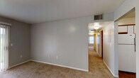 This single-floor residence offers a practical and comfortable layout designed for everyday living. The living room serves as the central gathering space, finished with neutral-toned carpet and featuring a large sliding glass door fitted with vertical blinds that allows natural light to filter in. An entryway door and open sightlines to the kitchen and a secondary room create a connected, open feel throughout the main living area.

The kitchen is well-appointed with white cabinetry trimmed in warm wood tones, gray laminate countertops, and a full suite of appliances including a refrigerator, electric range, built-in microwave, and dishwasher. A peninsula counter adds additional prep and dining space. Wood-style flooring extends through the kitchen and into the adjacent areas, providing a clean contrast to the carpeted rooms.

The bedrooms are carpeted and finished in neutral gray tones, each featuring a window with blinds for natural light and a dedicated closet with a hanging rod for storage. The bathroom includes wood-style flooring, a white vanity with cabinet storage, a wall-mounted medicine cabinet, and a full tub-shower combination, offering a clean and functional design throughout.