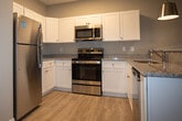 Located at 1718 Sherwood St in Greensboro, NC, this single-floor residence offers a thoughtfully designed layout with modern finishes throughout. The open-concept kitchen serves as a central hub, featuring white shaker cabinetry, granite countertops, a full suite of stainless steel appliances including a refrigerator, range, microwave, and dishwasher, and a peninsula island with pendant lighting overhead. A skylight adds natural brightness to the kitchen area, which flows seamlessly into the spacious living area finished with light wood-tone flooring. The bedrooms are generously sized, each benefiting from natural light through white-shuttered windows. The primary bedroom includes direct access to a private bathroom, along with closet space. The bathrooms are well-appointed, featuring granite-topped white vanities and tub-shower combinations. One bathroom stands out with elegant large-format marble-style tile flooring, adding a refined touch. Neutral gray-toned walls are carried throughout the home, contributing to a clean, cohesive aesthetic. The consistent light wood flooring, white trim, and ceiling fans complete the overall look, creating a bright, functional, and comfortable living environment.