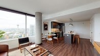 This thoughtfully designed high-rise residence offers a contemporary open-concept layout distinguished by expansive floor-to-ceiling windows that frame sweeping city skyline and water views throughout. The living area centers around rich hardwood flooring, a structural exposed concrete column—an architectural hallmark of the space—and generous natural light streaming in from multiple directions. The kitchen is a standout feature, equipped with sleek dark cabinetry, a large island with a white quartz countertop and undermount sink, stainless steel appliances including a professional-grade gas range and French door refrigerator, and polished pendant lighting overhead. A dedicated dining area sits adjacent to the kitchen, completing the open social layout.

The two bedrooms are carpeted for comfort, each offering direct window access to the elevated views outside. Both bathrooms are finished in a clean, modern aesthetic with white quartz countertops, undermount sinks, grey cabinetry, and large-format tile flooring. One bathroom features a dual-sink vanity. A half bath provides additional convenience for guests. The overall ambiance is modern, sophisticated, and light-filled throughout.
