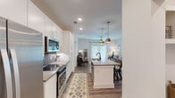 This single-story residence in Greenville, SC offers a thoughtfully designed open-concept layout with contemporary finishes throughout. The kitchen serves as a central hub, featuring white cabinetry with gold hardware, a herringbone tile backsplash, stainless steel appliances, and a large center island with a quartz countertop, undermount sink, and bar seating. Pendant lighting with brass fixtures adds a warm, modern touch. Wood-look flooring flows seamlessly through the kitchen, dining, and living areas, creating a cohesive aesthetic.

The living and dining spaces are well-lit, benefiting from natural light through large windows. Two bedrooms feature plush carpeting, ceiling fans, and generous window treatments. The primary bedroom connects to a well-appointed bathroom with a dual-sink vanity, quartz countertops, gold-accented hardware, and a glass-enclosed shower. A spacious walk-in closet with built-in shelving and hanging systems provides ample storage.

A second full bathroom includes a subway tile tub-surround, wood-look flooring, and a clean white vanity. The overall design balances modern style with functional, comfortable living throughout.