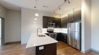 Located at 120 South 5th Street in Nashville, TN, this well-appointed 2-bedroom, 2-bathroom residence offers a thoughtfully designed open-concept floor plan. The kitchen serves as a central hub of the living space, featuring dark espresso cabinetry, a white quartz peninsula with an undermount sink, stainless steel appliances including a range, microwave, dishwasher, and refrigerator, along with a classic white subway tile backsplash. Pendant lighting and a track lighting system illuminate the space, while hardwood-style flooring runs throughout the main living areas, adding warmth and continuity. The living room is bright and open, benefiting from natural light and direct access to a private balcony through sliding glass doors, offering outdoor views of the surrounding greenery and Nashville skyline. Both bedrooms are carpeted and generously sized, each featuring large windows that invite natural light and views of the outdoors. The two bathrooms are finished with large-format tile flooring, dark cabinetry with quartz countertops, and full tub-shower combinations with white tile surrounds. Each bathroom provides access to a dedicated closet equipped with wire shelving systems for organized storage. The overall ambiance is clean, modern, and move-in ready.