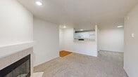 This single-floor residence offers a functional and well-organized layout across two bedrooms and two bathrooms. The open living room serves as the central gathering space, finished with wall-to-wall carpet and anchored by a tiled fireplace with a raised mantle. A large sliding glass door with vertical blinds fills the room with natural light and provides outdoor access. The adjacent kitchen is designed in a galley configuration, featuring white cabinetry, light countertops, a double-basin sink, and wood-look flooring. White appliances—including a refrigerator, stove, microwave, and dishwasher—are included. A pass-through counter connects the kitchen to the living area, enhancing the sense of openness. The primary bedroom is a comfortable size with carpet flooring and a dedicated closet with built-in shelving. The second bedroom is similarly finished with carpet and bright white walls. Both bathrooms are clean and simply appointed; one includes a single-sink vanity with mirrored cabinet, while the other features a tub-shower combo with sliding glass doors and wood-look flooring. A dedicated laundry area with washer and dryer hookups adds practical convenience.