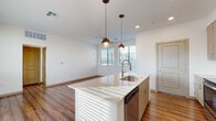 This single-floor unit offers a thoughtfully designed, modern living space defined by clean lines, neutral tones, and warm hardwood-style flooring that flows seamlessly throughout. The open-concept kitchen and living area form the heart of the unit, creating a bright and functional space ideal for both everyday living and entertaining. The kitchen is well-appointed with a large center island featuring a built-in sink and quartz-style countertop, complemented by warm-toned cabinetry, a stainless steel French door refrigerator, a stainless steel range, and a built-in microwave. Pendant lighting above the island adds a stylish focal point, while recessed lighting provides ample illumination throughout. The adjacent living area benefits from natural light through horizontal-blind-fitted windows and is equipped with a ceiling fan for added comfort. A dedicated bedroom offers a calm, open retreat with a ceiling fan, natural light, and direct access to a closet. The bathroom is finished in a crisp, all-white palette featuring a quartz vanity with an undermount sink, sleek chrome hardware, a lighted mirror, and a full tub-shower combination with a window for natural ventilation. The overall ambiance is clean, contemporary, and move-in ready.