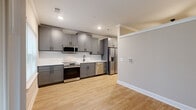 Located at 5672 Peachtree Pkwy in Peachtree Corners, Georgia, this thoughtfully designed single-floor unit offers an efficient and modern living experience. The space is defined by light hardwood-style flooring that runs throughout the main areas, neutral warm-toned walls, and crown molding that adds a refined touch to each room.

The kitchen is a standout feature, outfitted with gray shaker-style cabinetry, a clean white countertop, and a full suite of stainless steel appliances including a refrigerator with an ice and water dispenser, a range, a built-in microwave, and a dishwasher. Recessed lighting illuminates the space effectively, and a window at the end of the kitchen corridor brings in natural light.

Adjacent to the kitchen, an open living and dining area benefits from a large window and a sliding glass door that leads to a private balcony, offering views of the surrounding landscaped grounds and neighboring buildings. This connection to the outdoors enhances the overall sense of openness.

The bedroom features plush wall-to-wall carpeting and crown molding, providing a cozy and comfortable retreat. The bathroom is finished with matching gray cabinetry, a white countertop vanity, black hardware accents, and wood-look tile flooring, maintaining a cohesive and contemporary aesthetic throughout the unit.