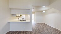 This two-story residence offers a well-organized layout with a blend of practical features throughout. The main living area is anchored by an open-concept design, where a peninsula-style kitchen connects seamlessly to the dining and living spaces. The kitchen is equipped with white cabinetry offering ample storage, a full suite of white appliances including a refrigerator, electric range, dishwasher, and a built-in overhead light fixture. A pass-through counter with a sink opens directly to the living and dining area, where a pendant light fixture adds a focal point overhead. Durable hardwood-style flooring runs throughout the main living spaces, while a separate room with hardwood-style flooring and a ceiling fan provides additional flexible living space. The bedrooms feature soft carpeting underfoot, with one bedroom offering dual windows that bring in natural light and a ceiling fan for comfort. Closet access is provided via dual doors. The bathroom includes a full-size soaking tub with shower combination and clean white finishes throughout. The vaulted ceiling in one room adds a sense of height and openness to the overall layout.