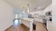 Located at 2250 Griffon Rd in Vero Beach, Florida, this single-floor residence offers a thoughtfully designed layout that maximizes functionality and comfort. The standout kitchen is outfitted with crisp white shaker cabinetry, gold-toned hardware, granite countertops, and a full suite of stainless steel appliances including a French door refrigerator, electric range, built-in microwave, and dishwasher. A peninsula with pendant lighting provides additional prep space and casual seating, while light wood-look flooring ties the area together with a clean, contemporary aesthetic. The living area flows naturally from the kitchen and features a ceiling fan and natural light from windows fitted with blinds. The generously sized bedroom is carpeted for comfort, features a ceiling fan, and connects directly to a dedicated walk-in closet with built-in shelving, offering ample storage. The bathroom echoes the home's design language with white cabinetry, granite countertops, gold hardware, a framed mirror, and wood-look flooring. Crisp white walls throughout the residence create a bright, neutral canvas. The overall ambiance is modern, clean, and move-in ready, making this Vero Beach residence an appealing and practical living space.