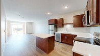 Located at 1875 Paulson Rd in River Falls, WI, this well-appointed one-bedroom, one-bathroom unit offers a thoughtfully designed single-floor layout. The open-concept kitchen and living area serves as the heart of the home, featuring rich cherry-toned cabinetry with sleek hardware, crisp white countertops, a central island ideal for meal prep or casual dining, and a full suite of stainless steel appliances including a refrigerator, dishwasher, microwave, and range. Light hardwood-style flooring runs throughout the main living areas, lending a clean, modern aesthetic and a sense of continuity. The living room area is bright and open, with access to natural light and views of the surrounding landscape. The spacious primary bedroom is carpeted for comfort, includes a generous walk-in closet, and features a window that invites natural light and outdoor views. The full bathroom is finished with matching cabinetry, a white countertop vanity, wood-style flooring, and a shower-tub combination. Neutral wall tones and recessed lighting throughout contribute to a fresh, move-in-ready ambiance well-suited for comfortable everyday living.