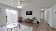 This single-story, 2-bedroom, 2-bathroom unit offers a well-organized layout across a compact but functional floor plan. The living room serves as the central gathering space, featuring wood-look laminate flooring, a textured ceiling with a ceiling fan and light fixture, and a sliding glass door flanked by vertical blinds that allows natural light to fill the room. The adjacent dining area connects seamlessly to the galley-style kitchen, which includes warm oak cabinetry, dark granite-style countertops, black appliances — including an electric range and built-in microwave — and matching wood-look flooring. The dining space accommodates a small table, making it suitable for everyday meals. The primary bedroom offers a comfortable footprint with plush carpet, a ceiling fan, a natural light window, and ample space for a full furniture arrangement. The second bedroom, also carpeted, features a notable vaulted ceiling with a skylight, adding brightness and a sense of openness. Both bathrooms are appointed with oak vanity cabinetry, wide mirrors, light countertops, and wood-look flooring. A hallway connects the bedrooms and bathrooms, maintaining a logical and efficient flow throughout the unit.