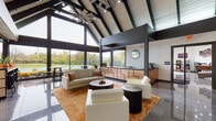 Located at 7800 Deer Creek Dr. in Columbus, Ohio, this contemporary single-floor clubhouse — known as the Park Club — delivers an impressive architectural experience from the moment you step through its sleek glass-and-dark-frame entry doors. The polished large-format tile flooring flows seamlessly throughout, reflecting light and enhancing the sense of openness across the entire space.

The centerpiece of the facility is a grand open lounge area defined by soaring vaulted ceilings with exposed dark structural beams and white shiplap panels overhead. A dramatic oversized starburst ceiling fan anchors the room, while floor-to-ceiling windows along an entire wall bathe the space in natural light and offer panoramic views of the surrounding greenery and outdoor pool area. Comfortable contemporary seating — including cream sofas and armchairs set over a warm amber area rug — surrounds dark accent tables, creating an inviting gathering atmosphere. A full-height white brick fireplace wall, complete with a linear electric fireplace and wall-mounted television, serves as a striking focal point on the opposite end of the lounge.

Adjacent to the lounge, a stylish reception counter with copper-toned geometric cabinetry provides a refined service area. A dedicated game room rounds out the amenities, equipped with a foosball table, skee-ball lane, pinball machine, wall-mounted television, and neon signage, offering vibrant entertainment options for all visitors.