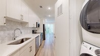 This well-designed single-floor unit offers a thoughtful layout across a comfortable footprint, blending modern finishes with functional living spaces throughout. Light wood-look flooring runs continuously through the main areas, creating a cohesive and airy feel.

The galley-style kitchen is outfitted with crisp white cabinetry, light quartz countertops, a subtle tile backsplash, and a full suite of stainless steel appliances including a range, microwave, dishwasher, and refrigerator. The kitchen opens directly toward the living area, which is bathed in natural light from large sliding glass doors and an additional window — both fitted with horizontal blinds. A ceiling fan with recessed lighting overhead completes the bright, open living space.

The bedroom is a well-proportioned retreat featuring the same wood-look flooring, a ceiling fan, recessed lighting, and sliding glass doors that offer outdoor views and additional natural light. An adjacent walk-in closet provides generous storage with wrap-around hanging rods and built-in corner shelving.

The bathroom showcases a clean, contemporary aesthetic with a marble-patterned surround tub and shower enclosure, white cabinetry with brushed gold hardware, a single-sink vanity with white countertops, and matching wood-look tile flooring. The overall design is clean, modern, and move-in ready.