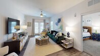 This single-floor residence showcases a thoughtfully designed layout that balances open communal spaces with comfortable private retreats. The kitchen is a standout feature, outfitted with sleek grey shaker cabinets, stainless steel appliances including a refrigerator, range, and microwave, and a generous granite-topped island with an undermount sink — ideal for both meal preparation and casual dining. Wood-style flooring flows throughout the main living areas, adding warmth and continuity.

The open-concept living room is bright and inviting, highlighted by a ceiling fan, French doors that draw in natural light, and ample space for comfortable seating. A decorative gold-framed mirror panel adds an artistic focal point near the entryway. The adjacent dining area features a bold navy accent wall framed in green, creating a vibrant, curated atmosphere.

Two well-appointed bedrooms provide restful retreats, each with plush carpeting, ceiling fans or soft lighting, and large windows dressed with curtains and blinds. The bathrooms are finished with granite countertops and wood-style flooring, with one featuring a tub-shower combination.

Throughout the space, a cohesive coastal-inspired color palette of navy, green, and white ties each room together, lending the home a fresh, lively, and welcoming character.