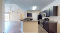 Located at 212 Katherine Blvd in Palm Harbor, Florida, this single-floor residence offers a well-designed, open layout with a seamless flow between living spaces. The kitchen is a standout feature, showcasing dark navy cabinetry, granite countertops, and a full suite of stainless steel appliances including a range, microwave, refrigerator, and dishwasher. A breakfast bar peninsula connects the kitchen to the main living area, which is finished with durable hardwood-style flooring and benefits from vaulted ceilings with ceiling fans that enhance the sense of openness. Sliding glass doors in the living area lead to a private balcony offering pleasant outdoor views of the surrounding Florida landscape, including lush palm trees. The bedrooms are carpeted for comfort and feature ceiling fans and windows that allow ample natural light. The bathrooms are finished consistently with dark vanity cabinetry topped with granite counters, wood-look flooring, and tiled tub-shower combinations with brushed nickel fixtures. Crown molding in the kitchen and living areas adds a refined touch throughout, while warm neutral tones create a cohesive and welcoming ambiance across the entire residence.