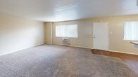 This single-floor residence offers a practical and functional layout across several well-defined spaces. The living area is generously proportioned, featuring neutral-toned carpet, a textured ceiling, and a ceiling fan with integrated lighting. A window unit provides climate control, and a large window with vertical blinds allows natural light to fill the room. The space opens toward a pass-through kitchen counter, creating a connected feel between the living and cooking areas.

The kitchen is equipped with white cabinetry, granite-patterned countertops, a stainless steel gas range, an under-cabinet range hood, and a double-basin sink. Warm hardwood-style flooring runs throughout the kitchen and bathroom, providing a clean contrast to the carpeted rooms.

The bedrooms are comfortably sized, each featuring plush carpet, ceiling fans, and windows with exterior views. Both rooms include mirrored sliding closet doors, with built-in shelving and hanging rods offering practical storage. One bedroom also provides direct access to an additional storage or utility area.

The bathroom includes a full tub-shower combination with a window above for natural ventilation, a granite-topped vanity with white cabinetry, and hardwood-style flooring, maintaining a cohesive design throughout the unit.