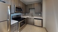 Located at 1 S Clinton Ave in the heart of downtown Rochester, NY, this single-floor unit offers a thoughtfully designed layout with modern finishes throughout. The open living area features light-toned luxury vinyl flooring that reflects natural light streaming in through the windows, creating a bright and airy atmosphere. The space incorporates varied ceiling heights with distinct architectural soffits, adding visual interest to the otherwise clean, neutral interior.

The kitchen is a standout feature, outfitted with dark wood-grain cabinetry, white quartz countertops, and a full suite of stainless steel appliances, including a range, microwave, and dishwasher. A gray subway tile backsplash adds a contemporary touch that complements the overall design palette.

The bedroom is a calm, carpeted retreat with natural light provided by a window with outdoor views. The bathroom is efficiently designed, featuring a single-sink vanity with a wood-tone cabinet, a glass-enclosed shower stall, and light vinyl flooring that ties the space together. An in-unit washer and dryer further enhance the functionality of this well-appointed urban residence.