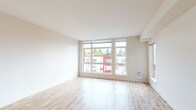 This well-designed single-floor unit offers a clean, contemporary aesthetic throughout. The open living area is a standout feature, characterized by large floor-to-ceiling windows that flood the space with natural light and provide views of the surrounding neighborhood. Light-toned hardwood flooring extends across the main living area, contributing to a bright and airy atmosphere with neutral wall tones that complement the modern design.

The kitchen is thoughtfully appointed with dark wood cabinetry, white quartz countertops, a tile backsplash, stainless steel appliances including an electric range and over-the-range microwave, and open upper shelving for convenient storage.

The bedroom areas feature plush carpet and are separated from the main living space by frosted sliding glass panel doors, offering both privacy and a sense of visual connectivity. A baseboard heating unit ensures year-round comfort. One bedroom provides direct access to a closet area.

The bathroom is generously sized, featuring a dual-sink vanity with dark wood cabinetry and white countertops, a large mirror, and tile flooring. A stacked washer and dryer unit is conveniently integrated within the bathroom space, and a separate water closet with a walk-in shower adds to the unit's functional layout.