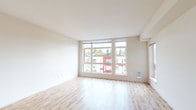 This well-designed single-floor unit offers a clean, contemporary aesthetic throughout. The open living area is a standout feature, characterized by large floor-to-ceiling windows that flood the space with natural light and provide views of the surrounding neighborhood. Light-toned hardwood flooring extends across the main living area, contributing to a bright and airy atmosphere with neutral wall tones that complement the modern design.

The kitchen is thoughtfully appointed with dark wood cabinetry, white quartz countertops, a tile backsplash, stainless steel appliances including an electric range and over-the-range microwave, and open upper shelving for convenient storage.

The bedroom areas feature plush carpet and are separated from the main living space by frosted sliding glass panel doors, offering both privacy and a sense of visual connectivity. A baseboard heating unit ensures year-round comfort. One bedroom provides direct access to a closet area.

The bathroom is generously sized, featuring a dual-sink vanity with dark wood cabinetry and white countertops, a large mirror, and tile flooring. A stacked washer and dryer unit is conveniently integrated within the bathroom space, and a separate water closet with a walk-in shower adds to the unit's functional layout.