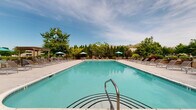 Located at Southgate Manor in Louisville, Kentucky, this outdoor community pool area offers a well-appointed recreational retreat designed for relaxation and leisure. The centerpiece is a generously sized rectangular swimming pool with crystal-clear, blue-tinted water, accessible via stainless steel entry rails and bordered by a wide, clean concrete pool deck.

Surrounding the pool, an extensive arrangement of lounge chairs and chaise lounges provides ample space for sunbathing and socializing. Teal patio umbrellas are positioned throughout the deck, offering shaded seating areas alongside tables and chairs. A decorative wooden pergola anchors one end of the deck, adding architectural character and a shaded gathering spot.

The pool area is enclosed by a black metal fence for safety and privacy, with mature trees and lush landscaping forming a natural green perimeter that creates a sense of seclusion. On one side, a single-story pool house with a covered entrance, brick columns, and a pitched shingle roof provides access to restrooms and amenities. The entry is managed through a gated walkway, reflecting a secure and well-maintained facility.

The overall ambiance is inviting and resort-like, with the combination of vibrant greenery, open sky views, and thoughtfully arranged outdoor furnishings making this a standout community amenity at Southgate Manor.
