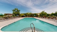 Located at Southgate Manor in Louisville, Kentucky, this outdoor community pool area offers a well-appointed recreational retreat designed for relaxation and leisure. The centerpiece is a generously sized rectangular swimming pool with crystal-clear, blue-tinted water, accessible via stainless steel entry rails and bordered by a wide, clean concrete pool deck.

Surrounding the pool, an extensive arrangement of lounge chairs and chaise lounges provides ample space for sunbathing and socializing. Teal patio umbrellas are positioned throughout the deck, offering shaded seating areas alongside tables and chairs. A decorative wooden pergola anchors one end of the deck, adding architectural character and a shaded gathering spot.

The pool area is enclosed by a black metal fence for safety and privacy, with mature trees and lush landscaping forming a natural green perimeter that creates a sense of seclusion. On one side, a single-story pool house with a covered entrance, brick columns, and a pitched shingle roof provides access to restrooms and amenities. The entry is managed through a gated walkway, reflecting a secure and well-maintained facility.

The overall ambiance is inviting and resort-like, with the combination of vibrant greenery, open sky views, and thoughtfully arranged outdoor furnishings making this a standout community amenity at Southgate Manor.