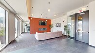 Located at 335 W Schiller St in Chicago's vibrant Old Town neighborhood, this amenity floor offers a thoughtfully designed collection of shared spaces suited for both relaxation and an active lifestyle. The lounge area serves as the heart of the floor, anchored by a bold terracotta accent wall housing a wall-mounted fireplace and flat-screen TV. A generous sectional sofa, globe pendant lighting, and large floor-to-ceiling windows create a warm yet contemporary atmosphere, with views of the Chicago skyline framing the space throughout. The fitness center is comprehensively outfitted with True-brand cardio equipment including treadmills and ellipticals, a cable machine, free weights, a squat rack, and an array of dumbbells. Floor-to-ceiling mirrors expand the space visually, while expansive windows provide abundant natural light and panoramic city views during workouts. The kitchen and dining area features a sleek, minimalist design with large-format grey tile flooring, flat-panel cabinetry, under-cabinet accent lighting, and a spacious island with seating for multiple guests. Pendant lighting overhead and access to natural light through nearby windows round out this functional yet refined space, ideal for entertaining or casual gatherings.