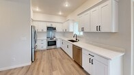 Located at 8801 Copperstone Ave SW in Lakewood, WA, this thoughtfully designed 2-bedroom, 2-bathroom unit offers a clean, modern aesthetic across a well-organized single-floor layout. Light wood-style luxury vinyl plank flooring flows consistently throughout, complementing the crisp white walls and black hardware accents that define the unit's contemporary style.

The kitchen is a standout feature, equipped with full stainless steel appliances including a refrigerator, range, over-the-range microwave, and dishwasher. White shaker-style cabinetry extends to the upper walls, providing generous storage, while white quartz countertops and a stainless steel backsplash complete the polished look. A window above the sink brings in natural light.

Both bedrooms are bright and comfortable, with large windows framing views of the surrounding neighborhood and mature trees. Each room includes closet space, with the primary bedroom offering a well-appointed en-suite bathroom featuring white vanity cabinetry, a quartz countertop, and matte black fixtures. The second bathroom includes a full tub-shower combo with similarly clean, modern finishes.

A central hallway connects all rooms efficiently and includes a dedicated in-unit laundry area with a stacked washer and dryer. The unit also features a patio, adding outdoor access to the overall living experience.