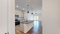 Located at 11124 Alexandriana Rd in Huntersville, NC, this well-appointed single-floor residence offers a thoughtfully designed layout with modern finishes throughout. The open-concept kitchen and living area serves as the heart of the home, anchored by a large center island with dark granite countertops and a matte black gooseneck faucet. The kitchen features crisp white shaker cabinetry with black hardware, a subway tile backsplash, stainless steel appliances, and stylish pendant lighting. The living area extends naturally from the kitchen and is bathed in natural light, with French doors providing outdoor access and a ceiling fan overhead. Warm hardwood-style flooring runs throughout the main living spaces, adding to the contemporary feel. The generously sized bedroom offers plush carpeting, a ceiling fan, and a bright window that fills the room with natural light. The bathroom is finished with a dark-framed vanity mirror, granite countertop, shaker-style cabinetry with black hardware, a glass-enclosed shower, and coordinating black fixtures. A dedicated laundry room with full-size washer and dryer and built-in shelving adds everyday convenience. A closet provides additional storage, completing this efficiently designed and stylish residence.