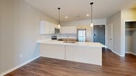 Located in the Starling community of Lincoln, NE, this well-designed 2-bedroom, 2-bathroom residence offers a comfortable and functional single-floor layout. The open-concept kitchen and living area serves as the heart of the home, featuring a large peninsula island with a white quartz countertop, undermount sink, and pendant lighting. The kitchen is fully equipped with stainless steel appliances — including a refrigerator, electric range, microwave, and dishwasher — complemented by a mix of white shaker and natural wood-tone cabinetry offering ample storage. Wood-style plank flooring runs throughout the entire residence, adding warmth and visual continuity. The living area is bright and open, with sliding glass doors leading to a private balcony with outdoor views. Both bedrooms are well-proportioned, with the primary bedroom featuring its own dedicated bathroom with a dual-sink vanity, light wood cabinetry, and a tub-shower combination. The second bathroom mirrors this clean, modern aesthetic with a full tub and shower. Each bedroom includes a closet, and neutral gray walls throughout create a versatile, move-in-ready canvas. Recessed lighting and abundant natural light complete the fresh, contemporary feel of this residence.