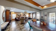 This leasing center in Birmingham, Alabama, offers a thoughtfully designed and welcoming environment that blends functionality with upscale interior design. The single-floor layout is organized into two distinct areas that flow seamlessly into one another.

The main lounge area serves as the centerpiece of the space, anchored by a dramatic sculptural chandelier crafted from layered, textured fragments that draws the eye upward toward the raised tray ceiling, which is accented with a bold orange finish. A curved brown leather sectional sofa, paired with an eclectic mix of patterned armchairs and drum side tables, is arranged atop a geometric-patterned area rug, creating a comfortable and visually engaging seating environment. Colorful wall art adds personality throughout. Large windows dressed with linen drapes and wooden blinds allow generous natural light to fill the room.

The reception area features a striking dark navy apothecary-style credenza topped with a coffee station and printer, flanked by decorative wall sconces and an ornate circular wall mirror. Adjacent to the reception desk, a private office with a desk and task chair provides a dedicated workspace.

A dining area with a round wood table and colorful mixed chairs offers additional meeting space, while French doors open to an exterior view, further enhancing the bright and open ambiance of this well-appointed leasing center.