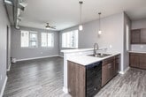Located at 550 9th St in Des Moines, Iowa, this 2-bedroom, 1-bathroom unit offers a well-designed single-floor layout with modern finishes throughout. The open-concept kitchen and living area serve as the heart of the home, featuring dark walnut-toned cabinetry, light quartz-style countertops, a double basin sink, and a full suite of black appliances including a range, microwave, dishwasher, and refrigerator. Stylish pendant lighting accents the kitchen, while the adjacent living area benefits from multiple windows with slatted blinds, a ceiling fan, and light wood-style plank flooring that flows throughout the main areas. The spacious primary bedroom offers generous room to furnish comfortably, complemented by a ceiling fan and natural light from a large window. The second bedroom also features a window, wood-style flooring, and convenient access to the hallway. Both bedrooms are supported by dedicated closets with wire shelving systems for organized storage. The full bathroom includes a combined tub and shower. Hallways connect the rooms with a clean, modern aesthetic, with exposed ductwork lending an industrial touch. The unit's neutral gray palette and consistent flooring create a cohesive, contemporary feel throughout.