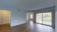 Located at 1900 Pineford Drive in Middletown, Pennsylvania, this single-floor residence offers a clean, functional layout with a welcoming open feel throughout. The main living area is a standout feature, showcasing rich hardwood-style flooring that runs continuously across the space, contributing to a warm and cohesive aesthetic. Neutral white walls provide a versatile backdrop suited to a variety of interior styles.

Natural light plays a significant role in the ambiance of the living area, which benefits from both a standard window and a full sliding glass door. The sliding door opens directly to an outdoor area, providing views of the surrounding greenery and seamlessly connecting the interior to the exterior. This feature also enhances ventilation and adds to the overall sense of openness within the space.

An adjoining room, visible through an open passageway, offers additional functional living space and features its own window, ensuring continued access to natural light. Overhead HVAC venting throughout indicates climate-controlled comfort year-round. The textured ceiling adds a subtle architectural detail to the otherwise understated interior design. Overall, the space presents a practical and bright single-level living environment.