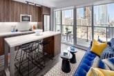 Located on the 16th floor at 8 Gloucester St in the heart of Toronto's Church-Wellesley Village, this thoughtfully designed one-bedroom, one-bathroom unit makes excellent use of its compact footprint. The open-concept living and dining area is anchored by expansive floor-to-ceiling windows that flood the space with natural light and frame striking panoramic views of the downtown skyline. Dark hardwood flooring runs throughout, complementing the clean, contemporary aesthetic. A sleek kitchen lines one wall, outfitted with wood-grain cabinetry extending to the ceiling, crisp white quartz countertops, an undermount sink, built-in stainless steel appliances including a wall oven, microwave, induction cooktop, and full-size refrigerator. A waterfall island provides additional prep and dining space. The bedroom is a bright, serene retreat featuring large sliding glass doors that open to a private balcony with unobstructed city views. The bathroom is finished with large-format grey wall tiles in the tub-shower surround, light porcelain floor tiles, a floating vanity with wood cabinetry, and a mirrored medicine cabinet. Clean white walls and recessed lighting throughout the unit contribute to an airy, modern ambiance ideal for urban living.